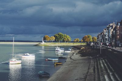 Boats moored on lake against cloudy sky