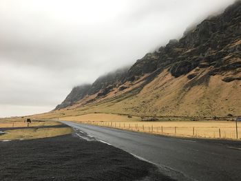 Country road by mountain against sky