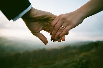 Cropped image of couple holding hands against sky