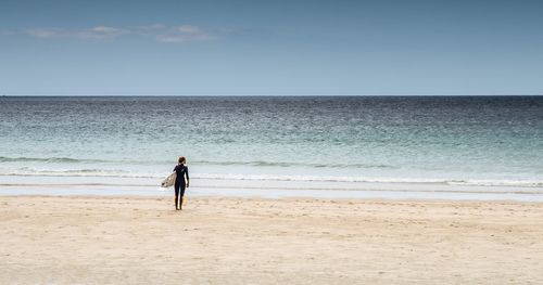 Woman with surfboard standing at beach against sky