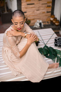 Side view of woman sitting on bed at home