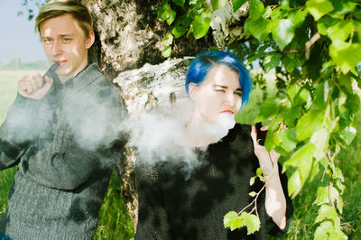 Friends smoking while standing by tree on field