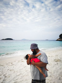 Father carrying daughter at beach against sky