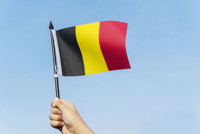 Cropped hand holding belgian flag against clear blue sky