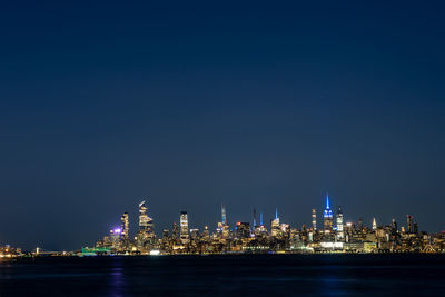 Illuminated buildings by sea against sky at night