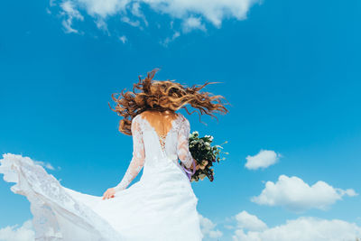 Low angle view of woman with bouquet standing against sky