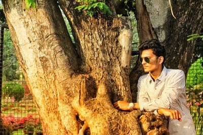 Young man in sunglasses leaning on tree trunk