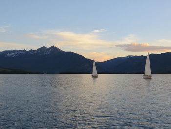 Sailboat sailing on sea against mountains during sunset