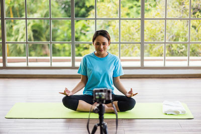 Full length of woman blogging while performing yoga against window