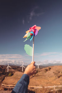 Cropped had of person holding pinwheel toy against sky