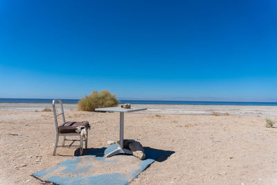 Chair on beach against clear blue sky