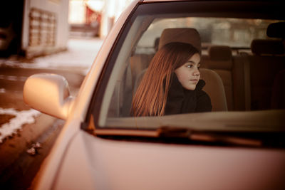 Girl looking away while sitting in car seen through windshield