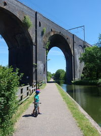 Man riding bicycle on bridge against sky