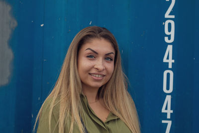 Portrait of smiling young woman standing against blue metal