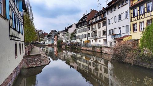 Canal in city against cloudy sky