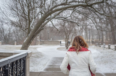 Woman walking on snow covered field against bare trees