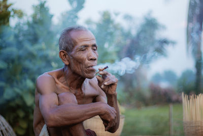 Shirtless man smoking while sitting outdoors