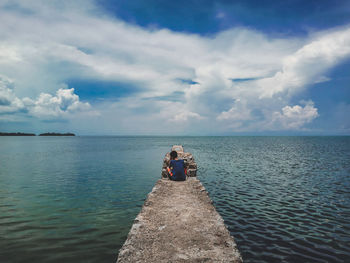 Rear view of boy sitting on stone wall by sea