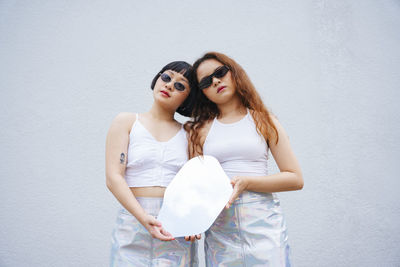 Portrait of lesbian couple holding mirror standing against wall