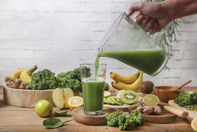 Man serving glass of green smoothie surrounded by ingredients