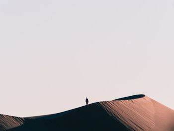 Low angle view of silhouette person standing on sand dune against clear sky