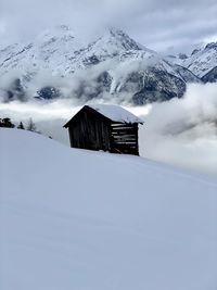 Barn on snow covered mountain against sky