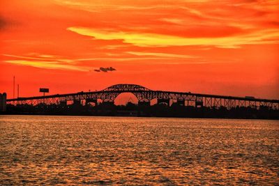 Silhouette bridge over river against orange sky