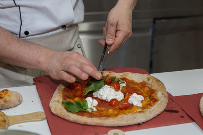 Pizza maker who prepares a delicious pizza with cheese, cherry tomatoes and basil.