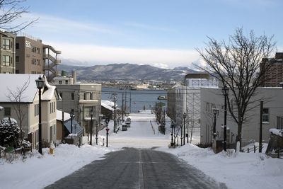 Snow covered road by buildings against sky