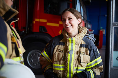 Smiling female firefighter looking at coworker while communicating in fire station