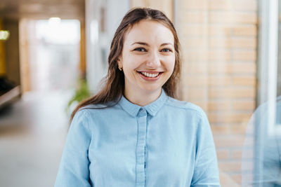 Portrait of happy young businesswoman standing at office corridor