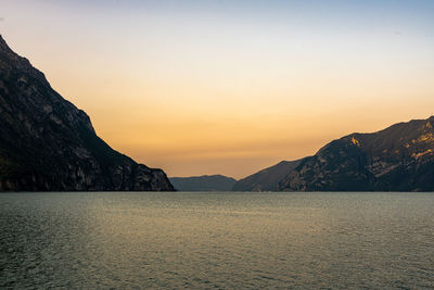 Scenic view of sea by mountains against sky during sunset