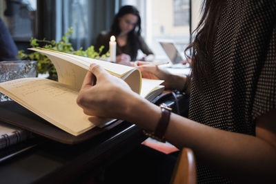 Midsection of woman turning pages sitting at table in creative office