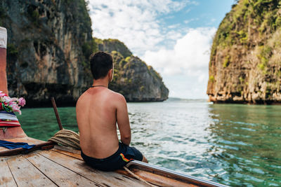 Rear view of shirtless man sitting on boat