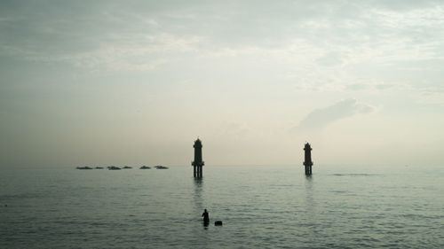 Silhouette people in sea against sky