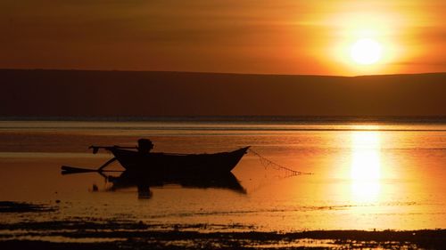 Silhouette man on boat in sea against orange sky