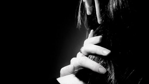 Cropped image of woman holding nail over black background