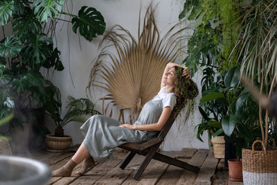 Satisfied calm woman florist relaxing in indoor garden enjoy mental balance and wellbeing at home