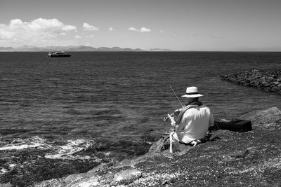 Rear view of woman sitting on shore against sky