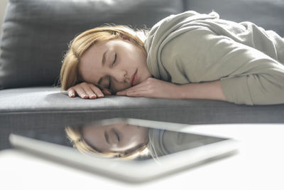 Close-up of woman lying on sofa reflecting in digital tablet