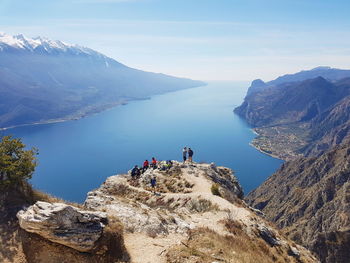 High angle view of people on rocks by sea and mountains against sky