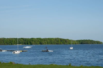 Boats sailing in lake against clear sky