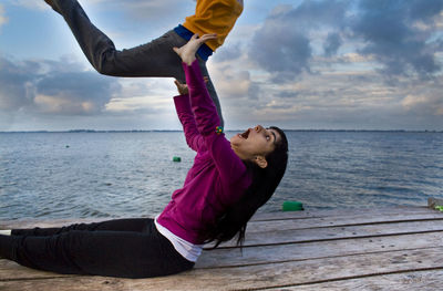 Optical illusion of woman lifting friend by sea