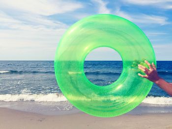 Cropped image of person holding inflatable ring at beach against sky