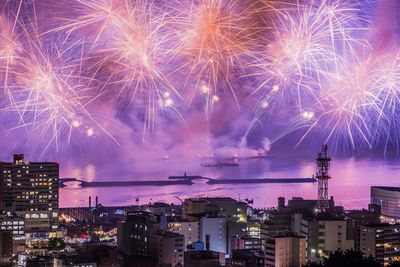 Firework display over city against sky at night