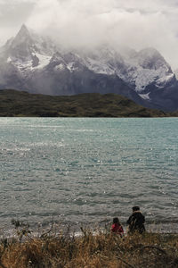 Rear view of people sitting by lake against mountains