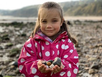 Portrait of girl smiling holding pebbles at beach