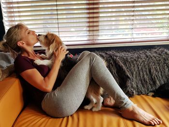Woman kissing dog on sofa at home