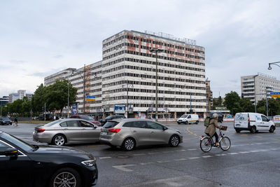 Cars on road by buildings in city against sky