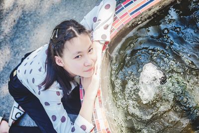 High angle portrait girl sitting by water fountain outdoors